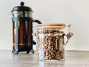 Glass jar of coffee beans next to French press filled with coffee