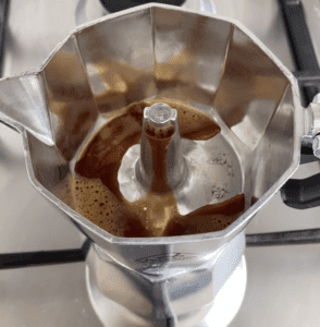 Picture showing a Moka pot brewing coffee with its lid open