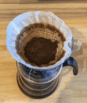 Image: V60 with filter papaer and dry, saturated coffee grounds sat on top of a glass carafe