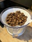 Image: V60 and filter paper on top of a ceramic mug, filled with coffee beans.