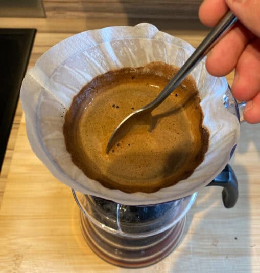 Image: V60 on top of a carafe, filled with coffee being stirred by a spoon