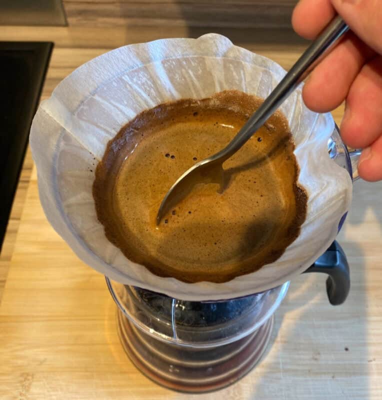 Image: V60 on top of a carafe, filled with coffee being stirred by a spoon